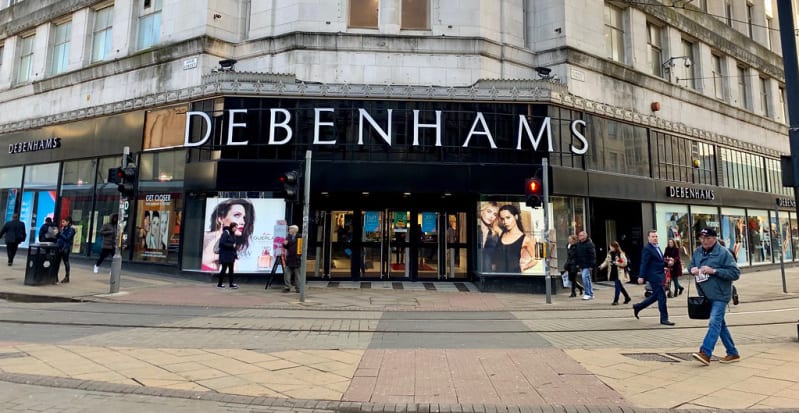 A picture of a Debenhams store on a street corner, with people walking past it.
