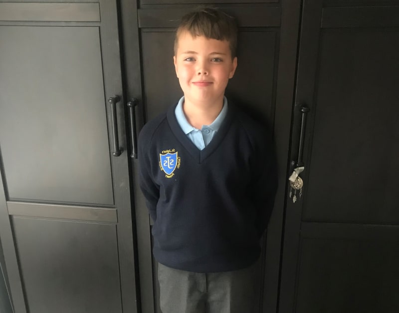 Jed is pictured in his school uniform standing in front of a set of wardrobe doors.